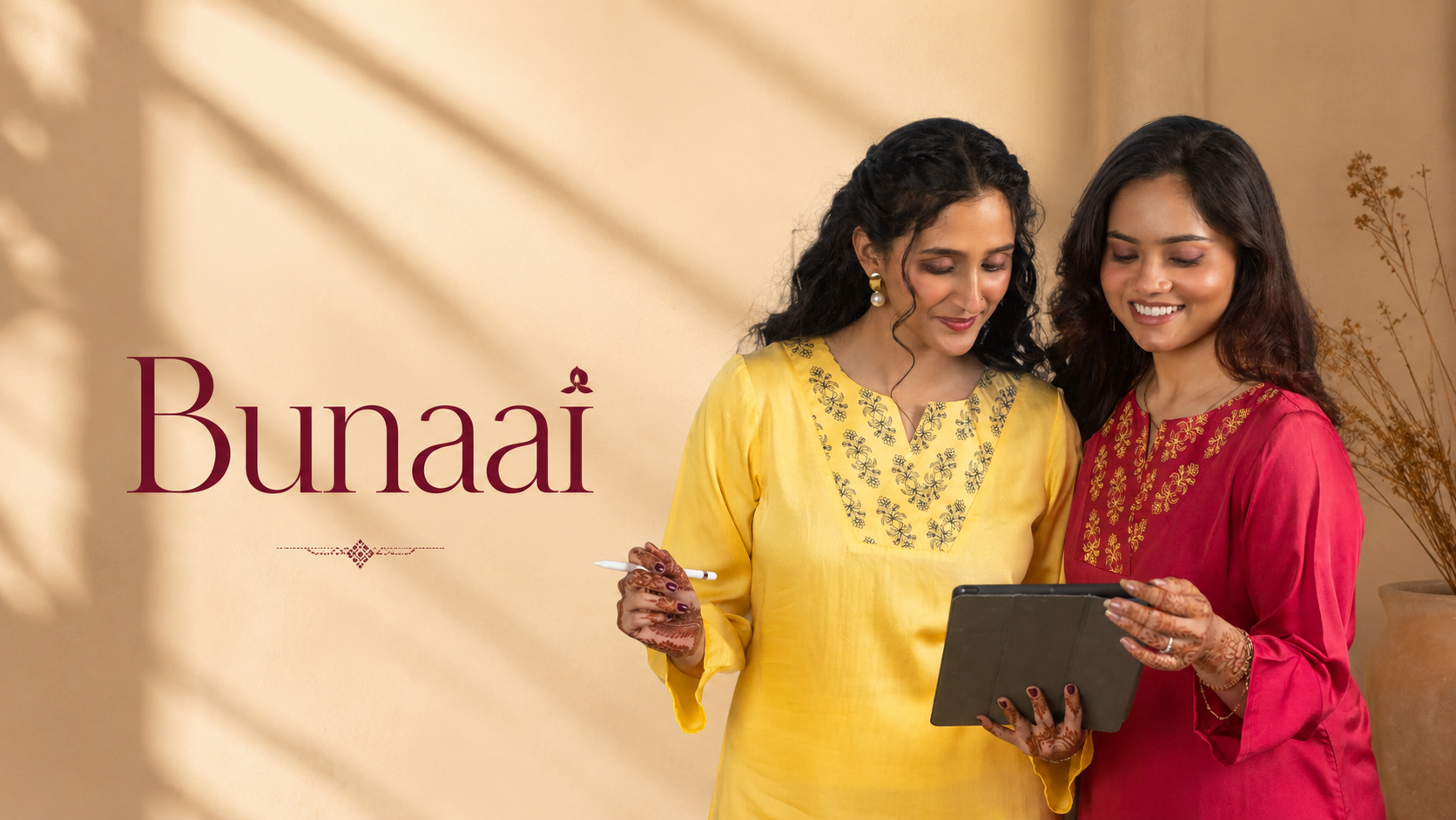Two women standing indoors wearing traditional Indian salwar kameez, one in yellow and one in pink, holding a tablet. The word 'Bunaai' is displayed on the left against a warm beige background with soft shadow patterns.
